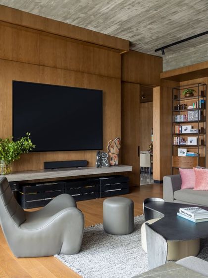 The TV lounge in the K Residence features a comfortable grey leather lounge chair and a sculptural coffee table from our Koko collection. The space is designed for casual relaxation, with a large screen and integrated sound system set against a warm wood-paneled wall.