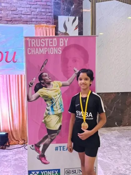 A champion's pose. Aarohi Salunke with her gold medal, standing next to a poster of her idol, PV Sindhu.