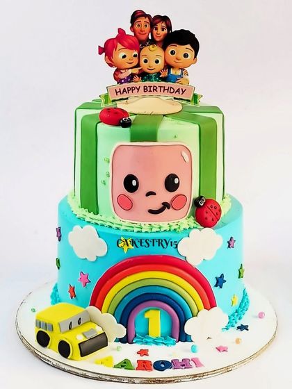 A classic two-tier Cocomelon cake with a rainbow and the iconic watermelon TV. This design is perfect for a first birthday, featuring the main characters and a yellow school bus.