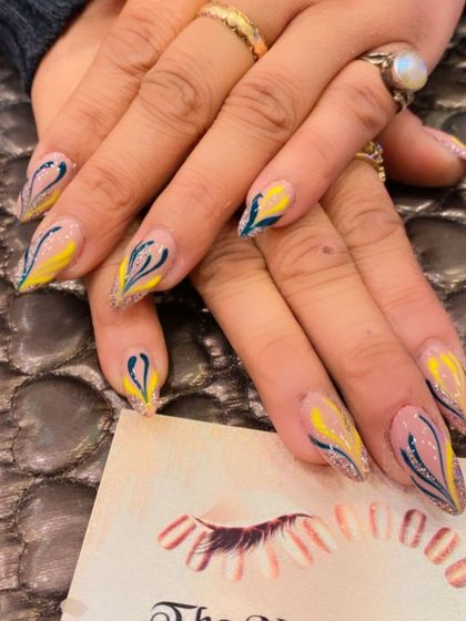 A beautiful and artistic design on long, clear stiletto nails. The nails feature an abstract pattern with yellow and dark blue strokes, accented with glitter.