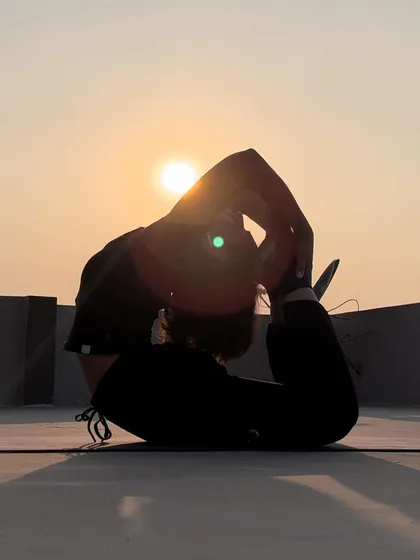 A sunset silhouette of Dhanurasana (Bow Pose). This powerful backbend opens the entire front of the body and strengthens the back muscles.
