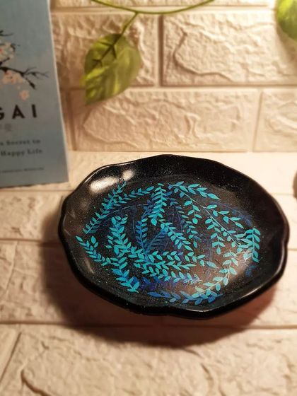 A close-up of our hand-painted leaves tray, showing the detail in the foliage design against the sparkling black background.