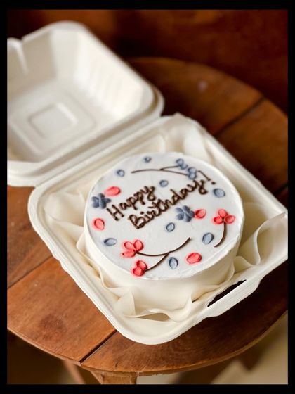 A pretty and simple birthday bento cake with delicate, hand-piped red and blue flowers on a clean white background.
