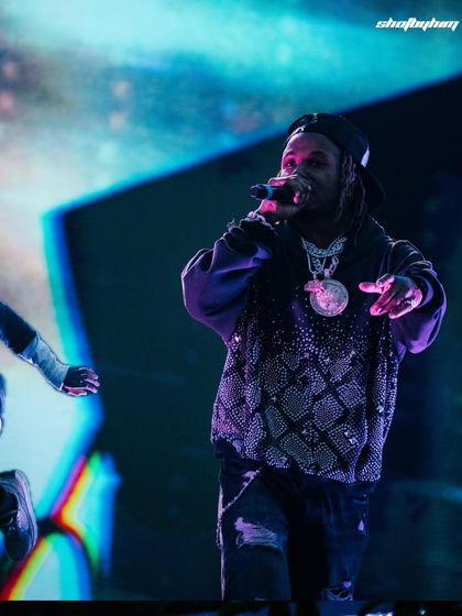Rich the Kid performing at Rolling Loud India, with a vibrant, abstract blue and purple background. The shot highlights the dynamic visual production of the festival.