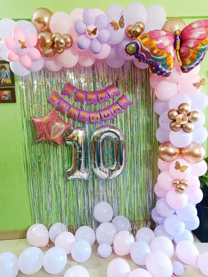 A delightful butterfly-themed 10th birthday party. The decor features a silver tinsel curtain, a pink and purple balloon arch, and large foil number balloons.