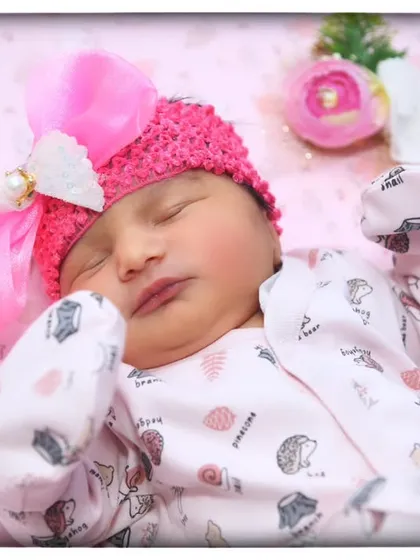 A close-up portrait of a sleeping newborn, showing the delicate details of her face and the soft pink bow in her hair.