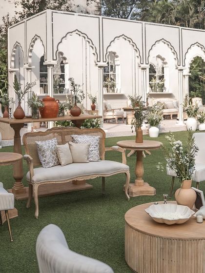 A comfortable and stylish guest seating area, combining natural wood and cane furniture with soft white upholstery, set against the Mughal-inspired backdrop.