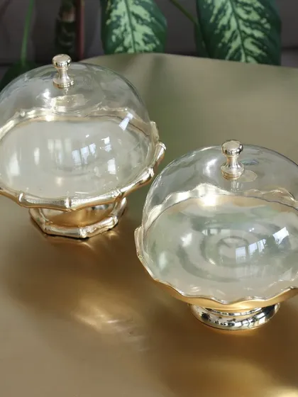 A pair of our gold dessert stands with glass cloches. The scalloped and bamboo-style bases showcase the variety in our collection, both designed to keep your treats fresh and beautifully displayed.