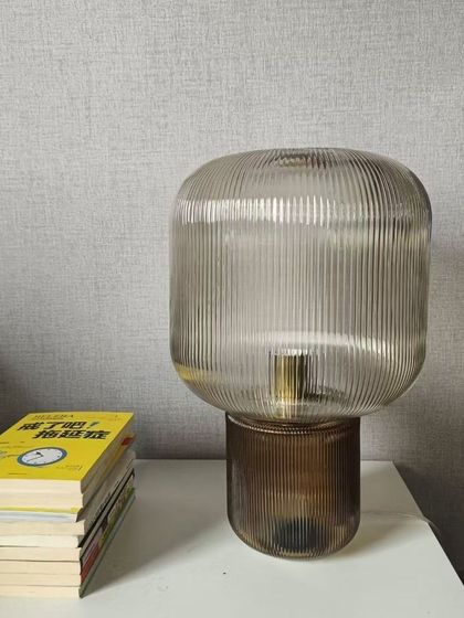 This Pirum table lamp features a ribbed glass design that creates a beautiful light effect, looking wonderful whether it is switched on or off. The smoked glass adds a touch of vintage charm to its modern shape.