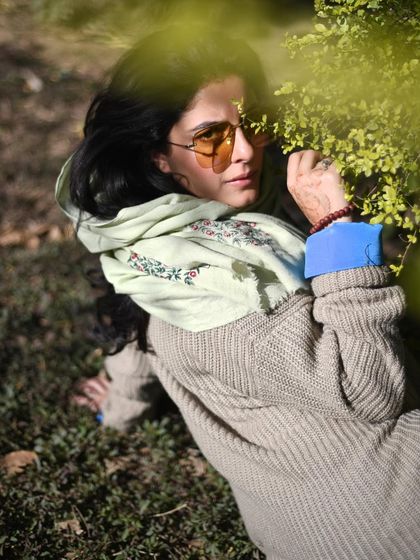 Isha Talwar lying in the grass, looking at the camera through sunglasses. The composition is playful and relaxed, perfect for an outdoor shoot.