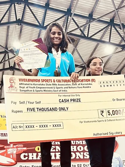 One of our top performers, Supriya, holding a cash prize check after winning four gold medals at the Tumkur open shooting competition.