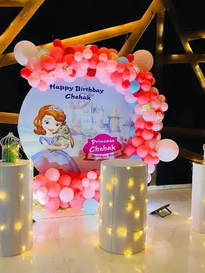 A magical "Princess Chehak" birthday party with a Sofia the First themed backdrop, a pink and red balloon arch, and illuminated pedestals.