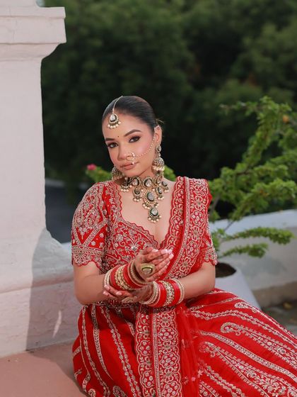 A candid moment of the bride, showing off the intricate jewelry and the detailed work on her red lehenga blouse.