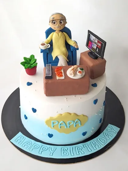 A cake for Papa's 80th birthday. The design features a custom figurine of him relaxing in his chair, watching TV with his favorite snacks.