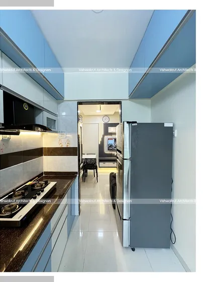 A galley kitchen layout for a 1BHK apartment. The design uses light blue and white cabinets to make the narrow space feel brighter and more open.