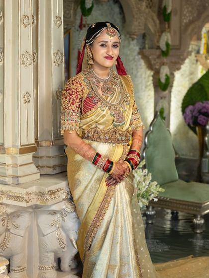 A full length view of the bride in her golden saree and red blouse, standing in a grand, ornate hall. The outfit is designed to make a statement and feel at home in the most luxurious of settings.