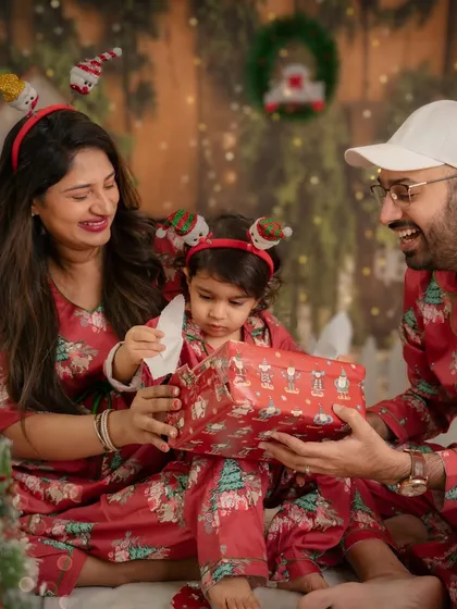 A little one carefully opens a Christmas present with their parents. The anticipation and excitement of the holidays are beautifully captured in this shot.