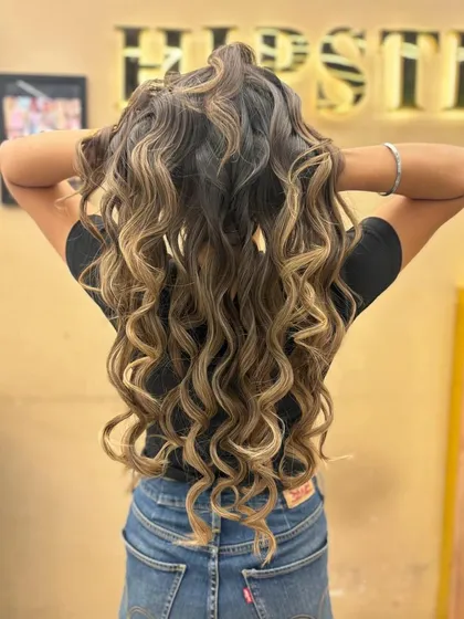 A stunning example of balayage on long, curly hair. The color enhances the texture and definition of the curls.