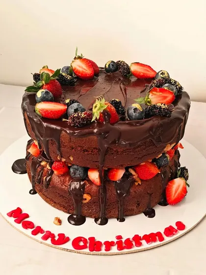 A festive "naked" Christmas cake, with layers of rich chocolate cake and frosting, dripping with chocolate ganache and topped with fresh berries.