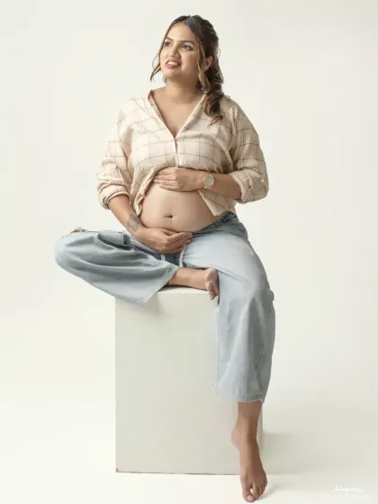 Seated comfortably on a studio block, this mom to be cradles her bump in a casual yet chic outfit. This pose is perfect for capturing a moment of quiet contemplation.