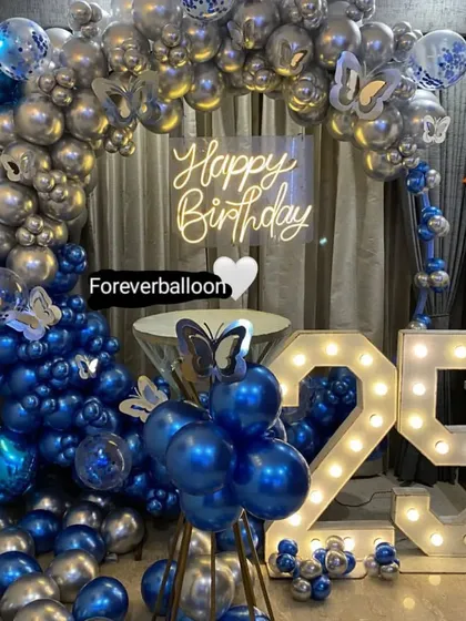 A stunning 25th birthday setup in royal blue and silver, with butterfly accents, a neon sign, and large marquee numbers.