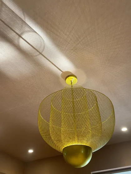 A golden mesh pendant light casts a web of beautiful shadows on the ceiling, turning a simple light fixture into a captivating feature.