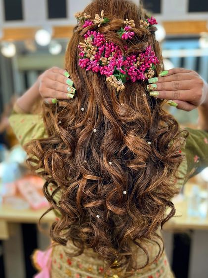 A full view of this intricate Mehendi hairstyle. The combination of braids, curls, pearls, and bold floral pieces creates a look that is truly unforgettable.