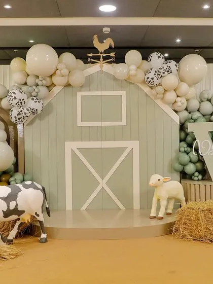 The full view of the modern farm backdrop, featuring a soft sage green and white color palette, cow-print balloons, and a custom monogram.