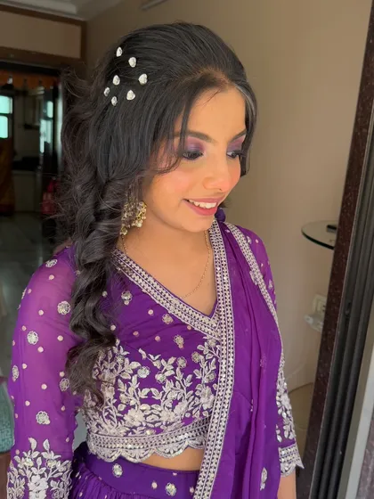 A close-up of a purple smokey eye and a braided, curly hairstyle. The pearl accessories in her hair add a delicate touch.