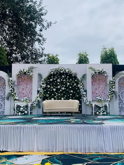 For this outdoor engagement, we designed a modern and elegant stage. The backdrop features intricate white jali panels, a central arch overflowing with white roses, and a clean, contemporary feel perfect for a sophisticated celebration.