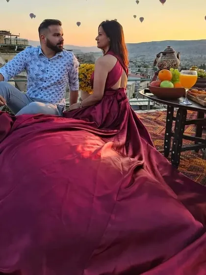 A couple enjoying a rooftop breakfast in Cappadocia. The bride is wearing my deep magenta trail gown, with hot air balloons dotting the sky behind them.