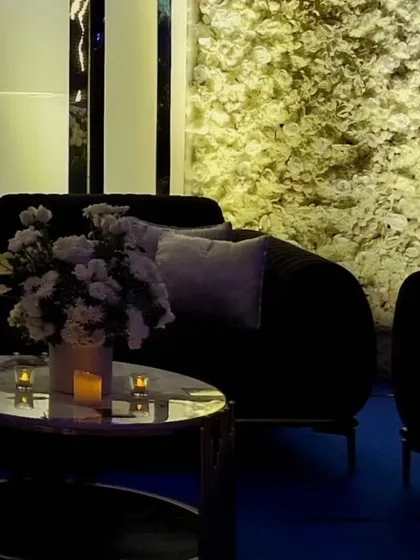 Another view of the lounge vignette, showing the contrast between the plush black sofa and the textured, illuminated flower wall.