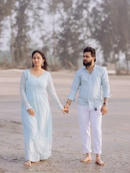 A full-length shot of the couple walking on the beach, capturing their coordinated outfits and the serene coastal environment.
