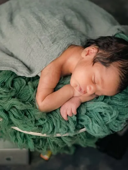 A top-down view of the 'Baby Director' setup, showing the newborn nestled comfortably in the green, textured basket, surrounded by professional camera gear.