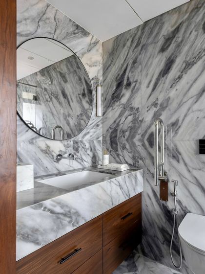 This bathroom in the Parishram residence features a different kind of marble, with bold, sweeping grey veins. A large, circular mirror and clean, modern fixtures complete the elegant design.