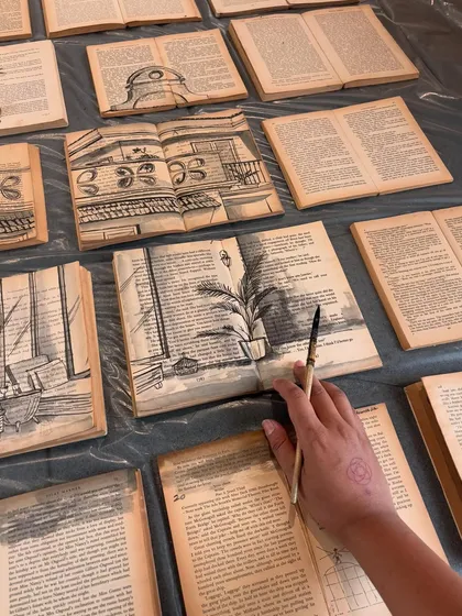 A process shot of 'The Villa between Pages', showing my hand adding details to the architectural sketches on the vintage book pages.
