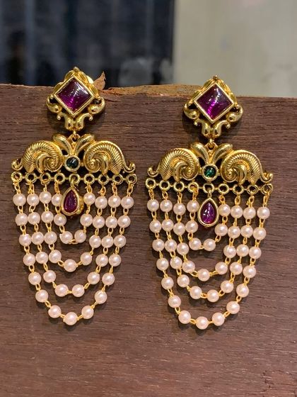 These elegant imitation earrings have a gold-look finish and feature beautiful cascading pearl drops. The top is adorned with a ruby-colored stone, making them perfect for festive occasions.
