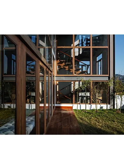 The exterior of the 'Aangan' house, where large glass panels reflect the surrounding landscape. The design focuses on an indoor-outdoor connection, using locally sourced timber to create a structure that feels both modern and rooted in its environment.