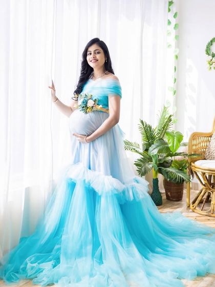 This light blue ball gown, with its ruffled skirt and floral belt detail, looks absolutely angelic in this bright, indoor setting. A perfect look for a classic baby shower or photoshoot.