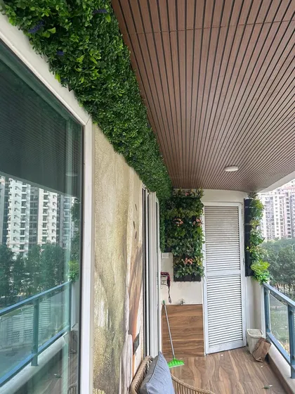 This balcony features artificial green panels used as a decorative border along the top and side walls, framing the space beautifully.