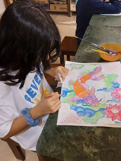 A student works diligently on her Japanese lucky carp painting. This multi-medium project for ages 8 to 15 combines watercolor backgrounds with detailed colored pencil work.