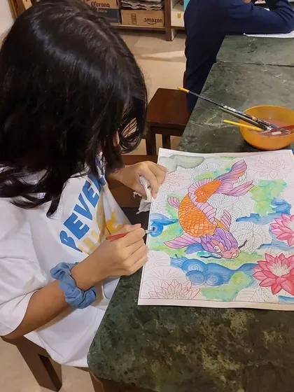 This student is carefully applying watercolor to her lucky carp design, a project that teaches both precision and color theory.
