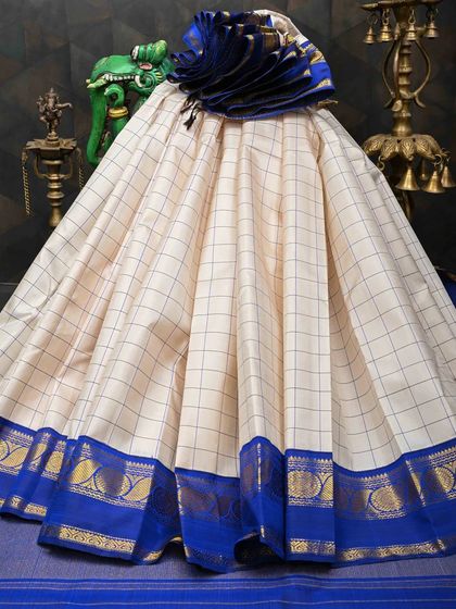 A classic cream Kanjivaram with a bold royal blue border and a simple check pattern. This is a timeless and versatile saree that can be dressed up or down.