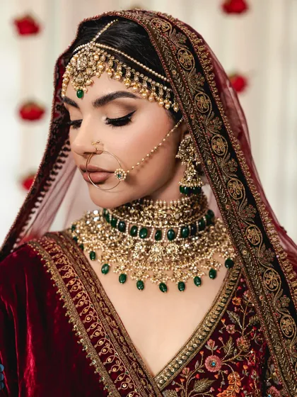 A stunning close-up portrait of the bride. Her traditional red velvet outfit is paired with a heavy polki and emerald necklace, a classic and regal combination.