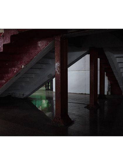 An abstract black and white photo focusing on the shapes and lines created by the underside of a staircase. The play of light and shadow creates a geometric and moody composition.