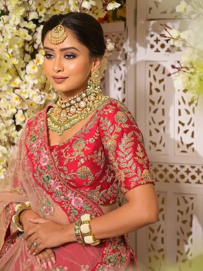 A beautiful portrait against a floral backdrop, highlighting the harmony between the bride's soft glam makeup and her intricately embroidered red lehenga. The look is traditional, elegant, and full of grace.