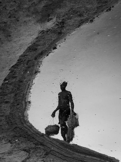 The reflection of a person carrying baskets is captured in a puddle, a clever black and white composition that plays with perception and reality.