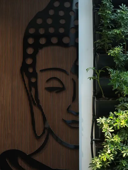 A modern, artistic interpretation of the Buddha is mounted on a wooden-paneled wall, right next to a thriving vertical garden, blending spirituality with contemporary design.