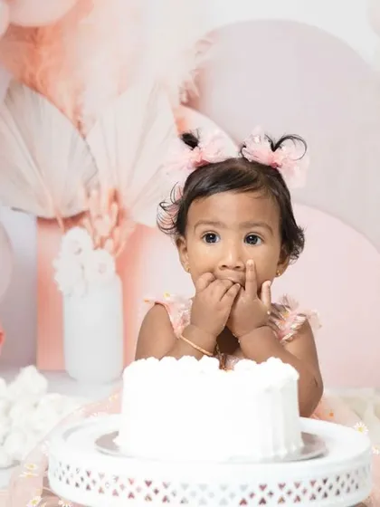 A sweet one-year-old girl enjoying her pink-themed cake smash session. I love capturing these close-ups of their frosting-covered fingers and happy faces.