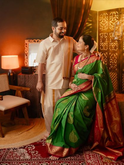 A loving couple portrait in a traditional setting. The partner stands supportively beside the seated mom-to-be, capturing their shared strength and connection.